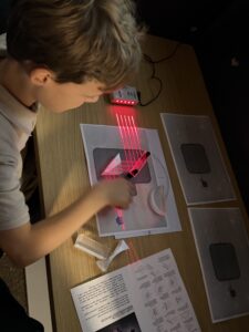 Een kindje verschuift een prisma, zodat rode laserstralen op een detector worden gemikt.