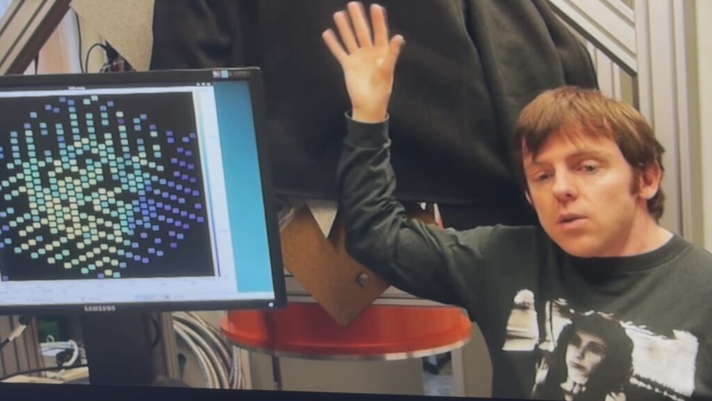 Een onderzoeker zwaait met zijn hand. Een detector kan dat dwars door verduisterende schermen heen toch detecteren en op een scherm zichtbaar maken.